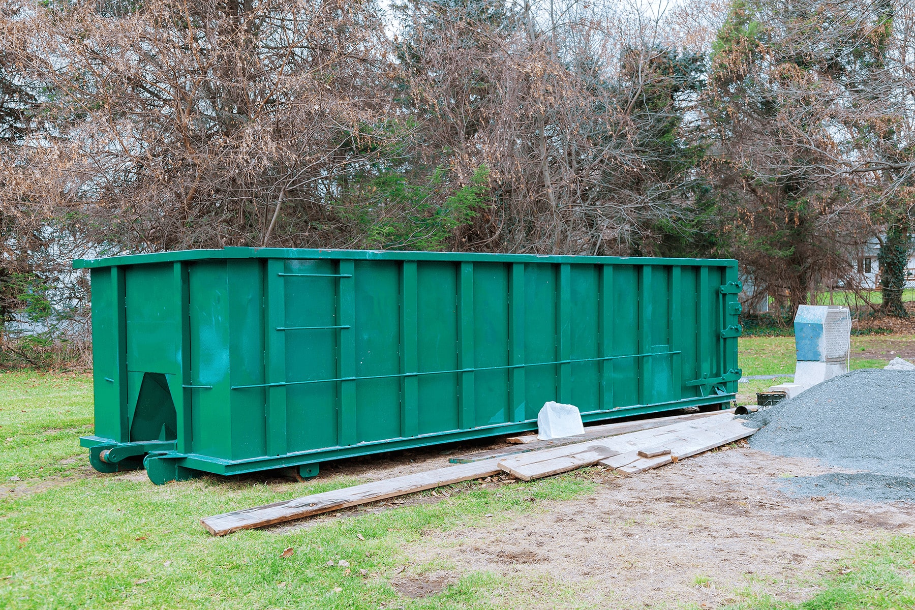 Large green roll-off dumpster on a grassy construction site.
