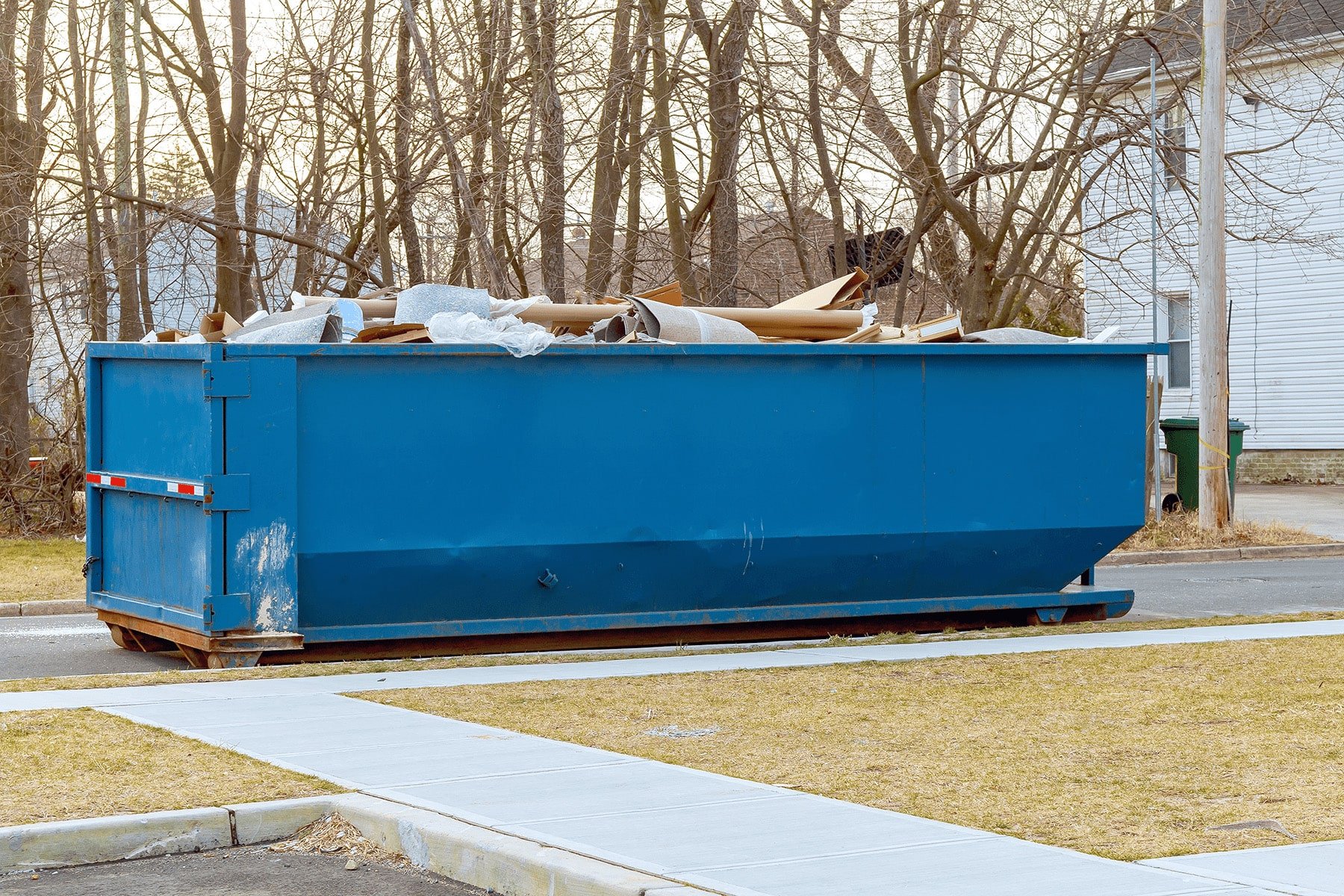 Blue roll-off dumpster placed near a sidewalk with debris inside.